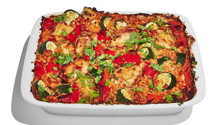 A baked casserole with layers of rice, courgette, red peppers, and herbs in a white baking dish.