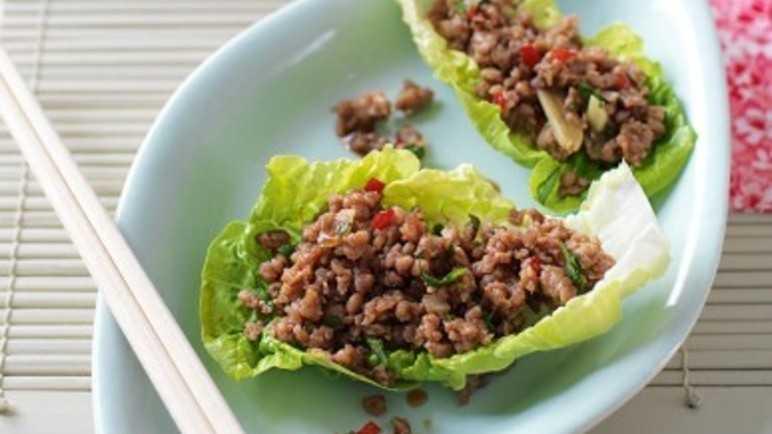 Lettuce wraps with seasoned ground meat are served on a light blue plate with white chopsticks alongside, an Asian-inspired meal.