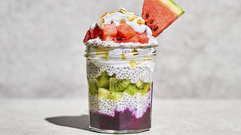 A layered fruit and yoghurt parfait in a clear glass jar, set against a plain background.