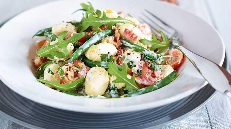Gnocchi with ricotta, bacon, tomato and beans, topped with fresh rocket and served on a white pasta plate.